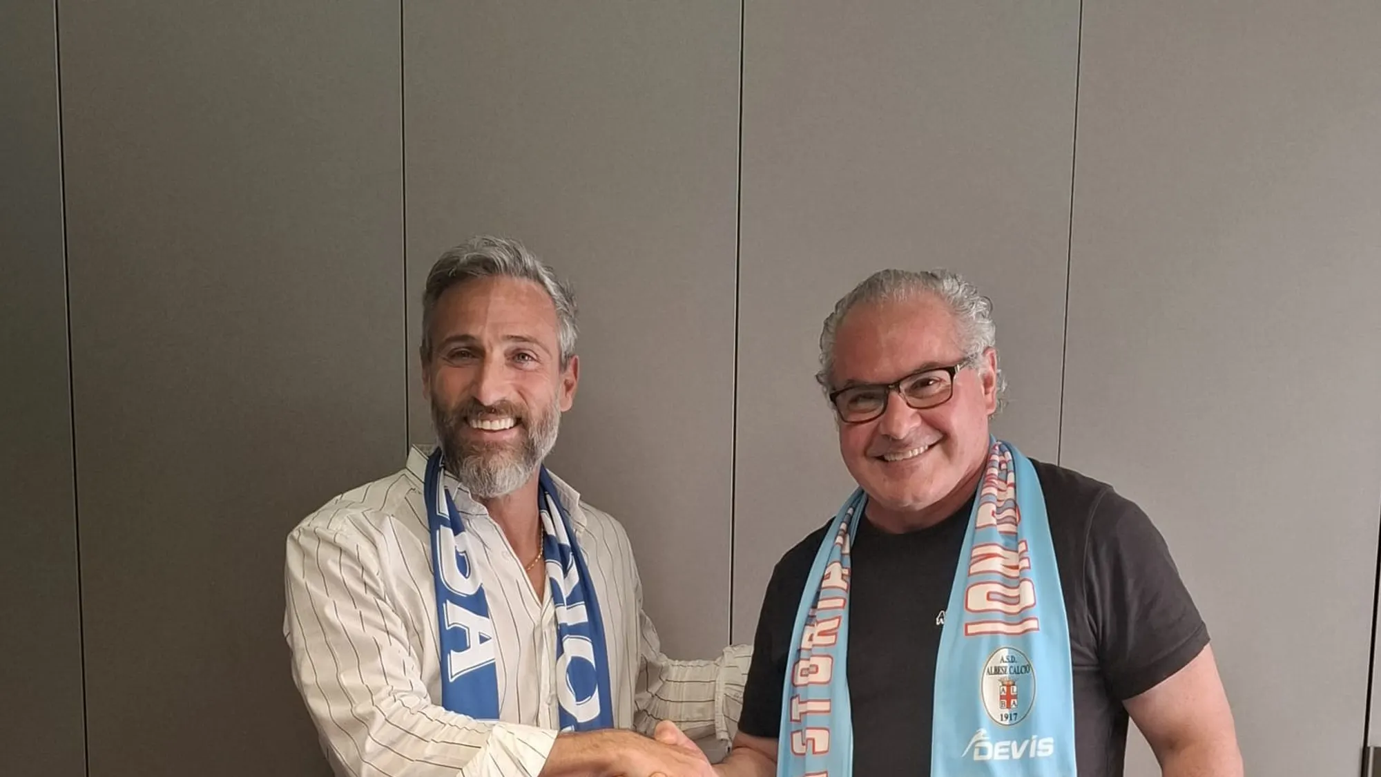 I dirigenti di Albese e Alba Calcio si stringono la mano, sul tavolo le maglie delle due società
