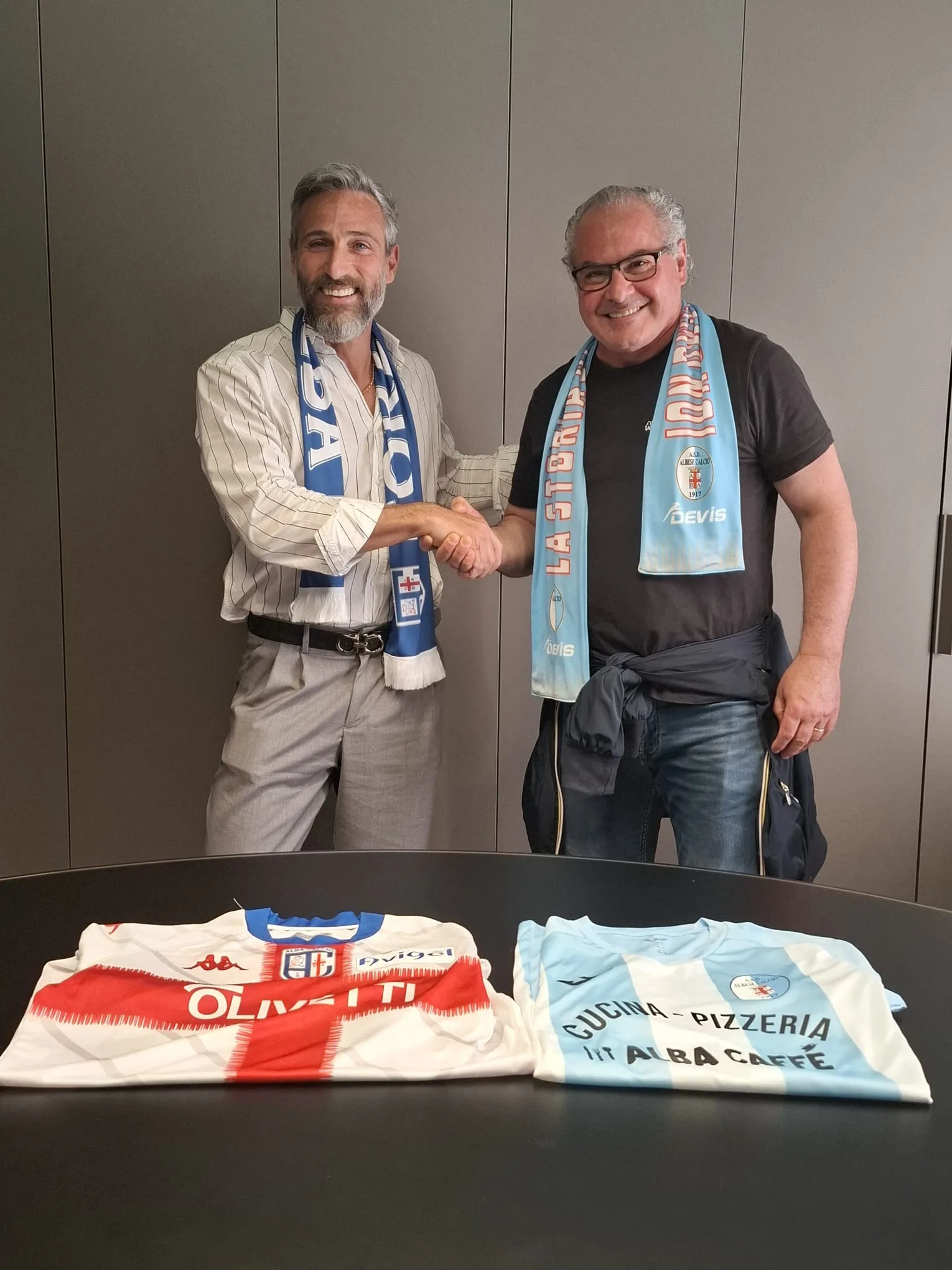 I dirigenti di Albese e Alba Calcio si stringono la mano, sul tavolo le maglie delle due società